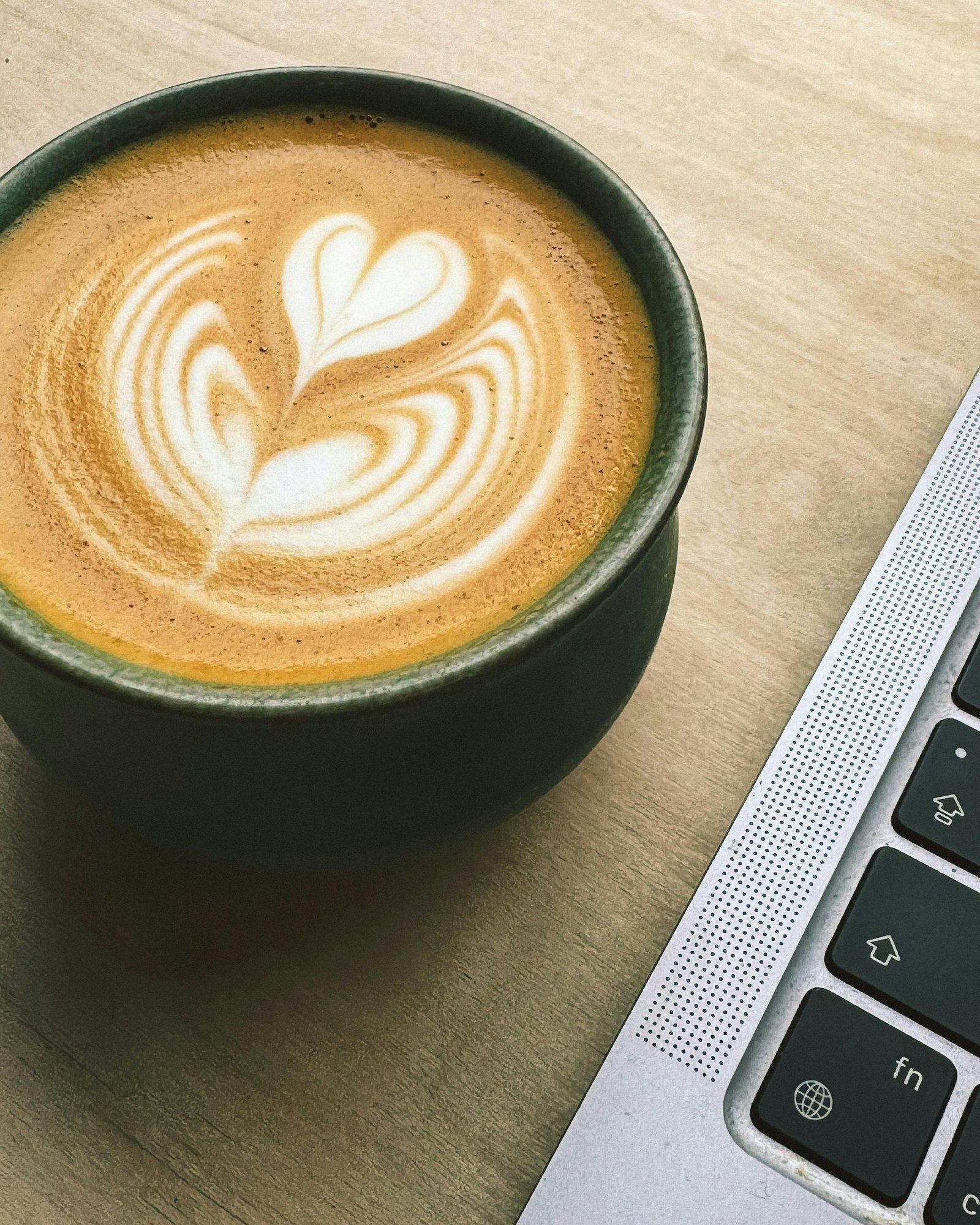 Een cappuccino op een houtkleurig bureau naast een laptop
